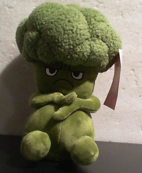Peluche de brócoli verde con expresión seria y brazos cruzados